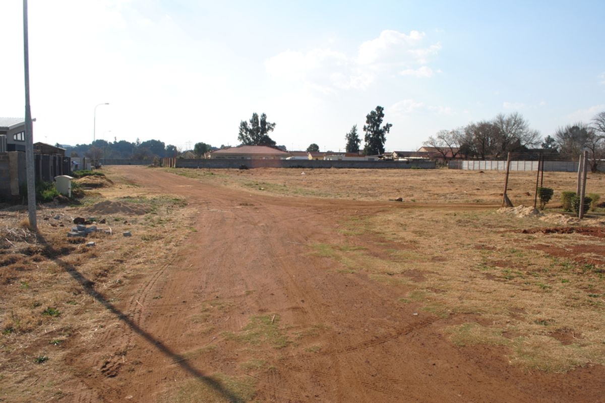 A view of a vacant residential plot featuring a dirt road and perimeter walling in a suburban setting.