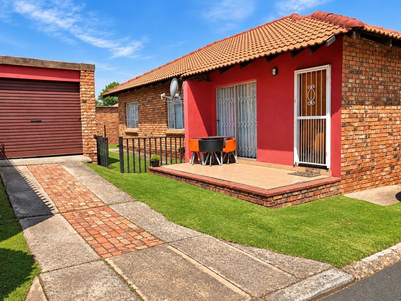 A well-maintained single-story brick house featuring a tiled roof, a paved driveway, an attached garage, and a front patio area.