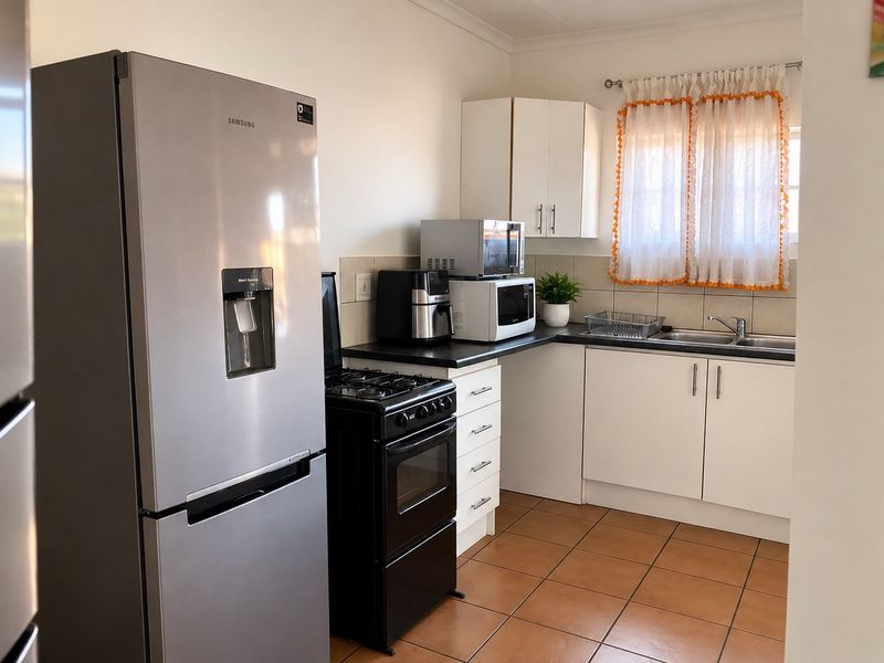A functional kitchen featuring white cabinetry, dark laminate countertops, a double basin sink, and tiled flooring, providing a practical workspace.
