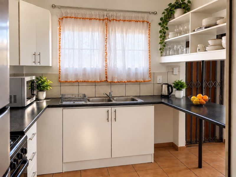 A functional kitchen featuring white cabinetry, dark laminate countertops, a double bowl stainless steel sink, and open shelving with tiled flooring.