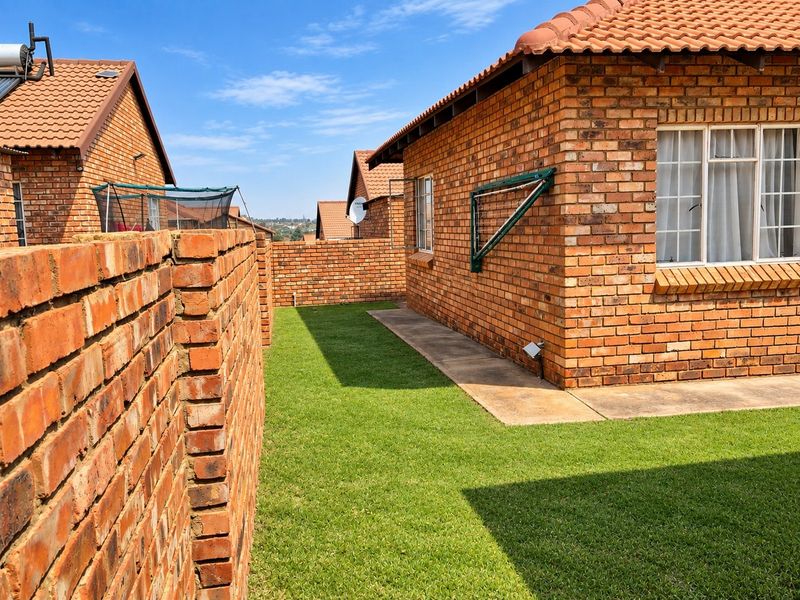 A side view of the property featuring a face brick exterior, tiled roof, concrete walkway, and a well-maintained lawn area.