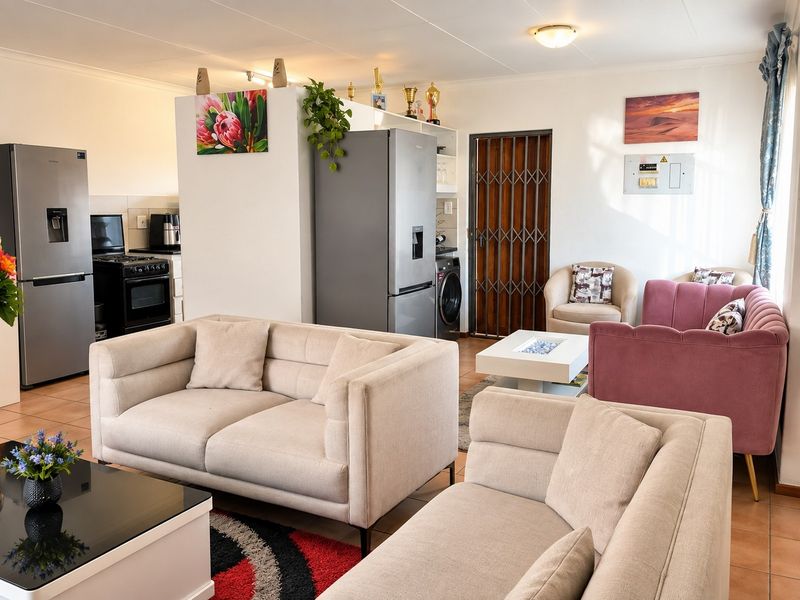Open-plan living area featuring tiled flooring, a functional kitchen space with built-in cabinetry, and direct access to a secure entrance.