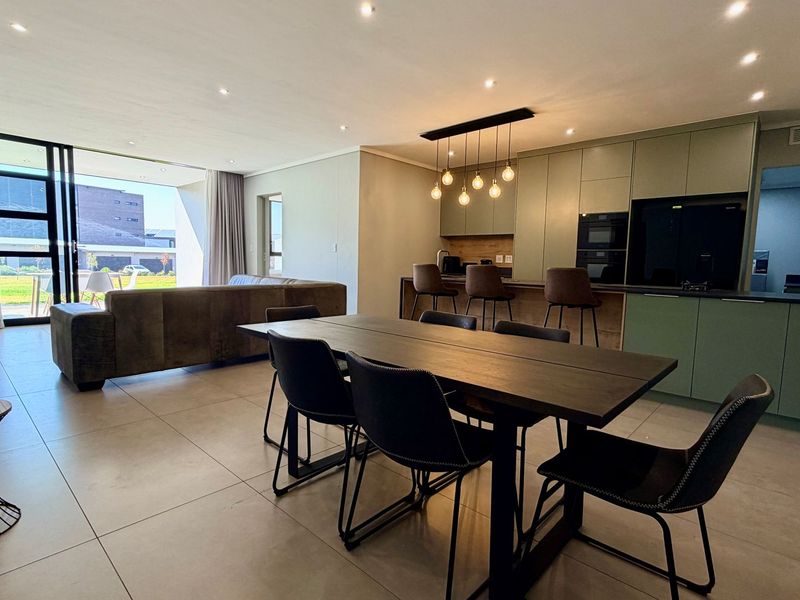 Modern open-plan living area featuring a contemporary kitchen with integrated appliances, tiled floors, and large sliding doors leading to an outdoor space.