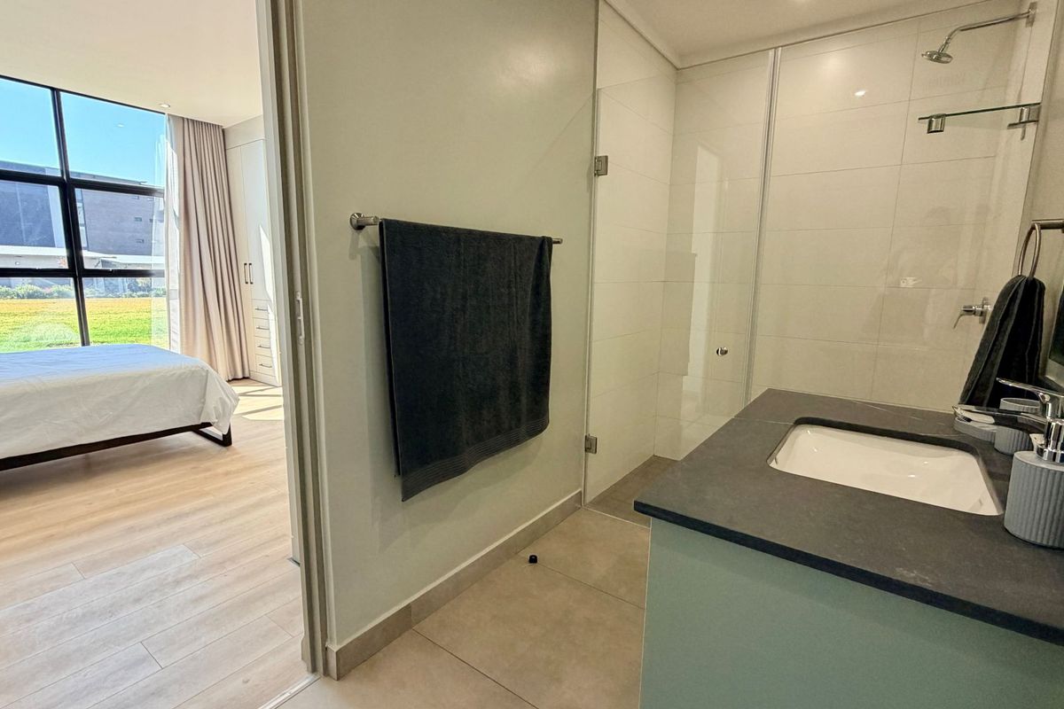 Modern en-suite bathroom featuring a walk-in shower with glass screen and a sleek vanity with stone countertop, adjacent to the bedroom.