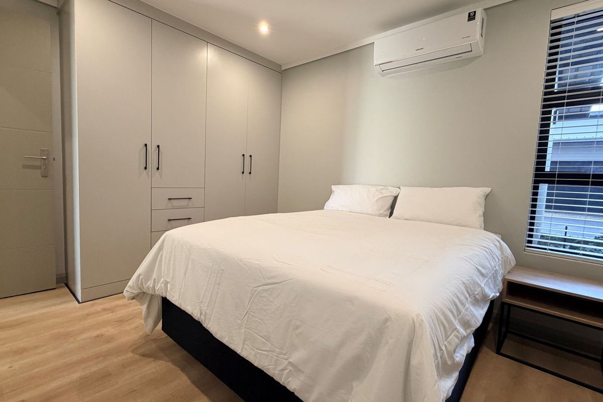 A modern bedroom featuring built-in cupboards, laminate flooring, and a wall-mounted split-system air conditioner.