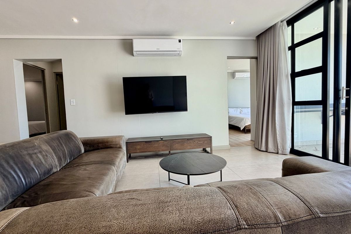 A modern, well-lit living room featuring tiled floors, a wall-mounted air conditioning unit, and large sliding glass doors leading to an outdoor area.