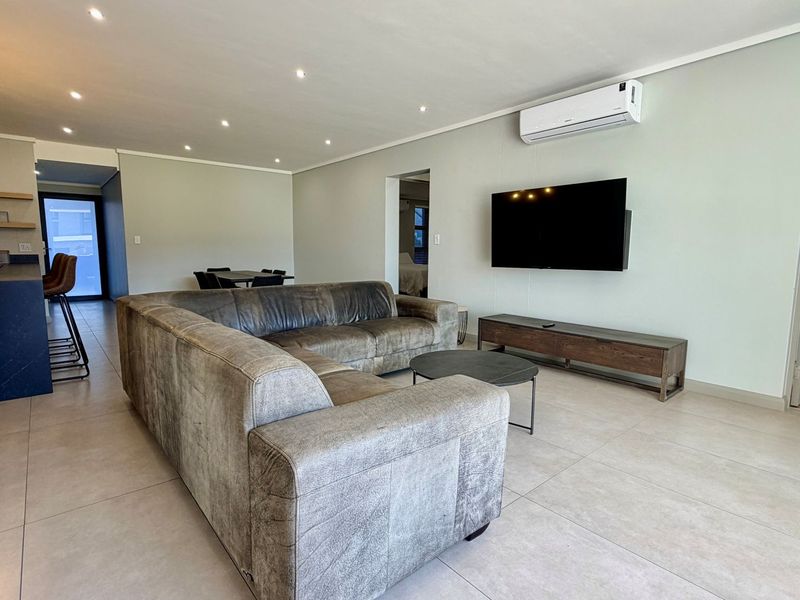 Spacious open-plan living area featuring modern tiled flooring, recessed downlighting, and a wall-mounted air conditioning unit, seamlessly connecting to the kitchen space.