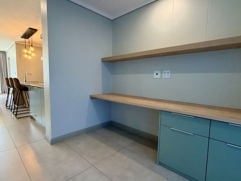 Modern open-plan living area featuring a dedicated built-in workspace with floating shelves and cabinetry, adjacent to a sleek kitchen with island seating.