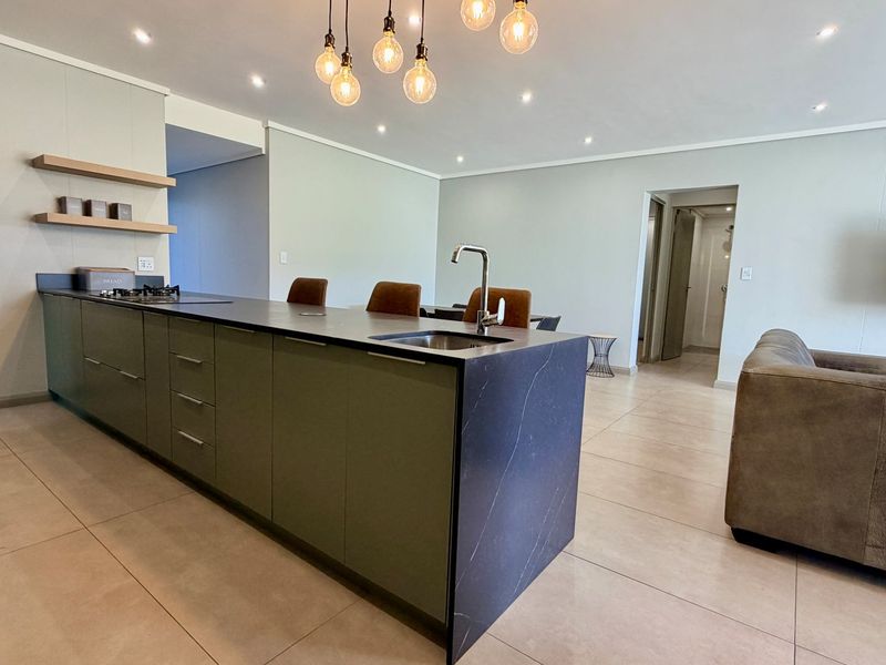 Modern open-plan living area featuring a sleek kitchen island with stone countertops, integrated hob, and contemporary pendant lighting, seamlessly flowing into the lounge space.