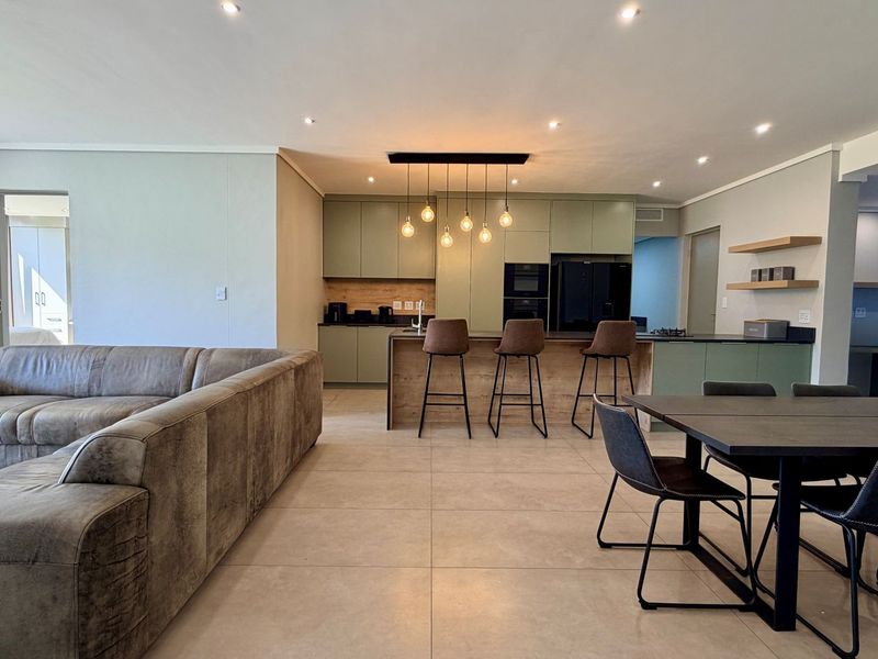 Modern open-plan living area featuring a contemporary kitchen with island, sleek cabinetry, and tiled flooring, seamlessly integrated with the dining and lounge space.