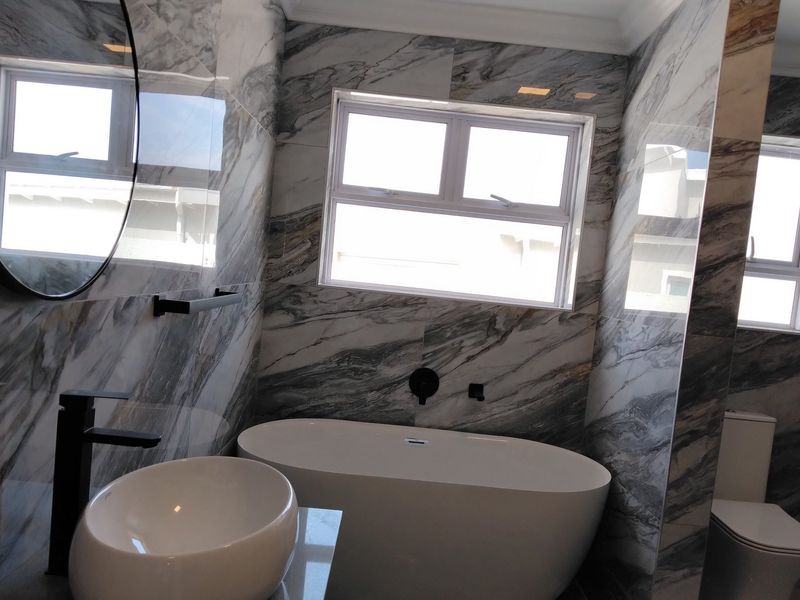 Modern bathroom featuring marble-look wall tiles, a sleek freestanding bathtub, a vessel sink with wall-mounted faucet, and a contemporary toilet.