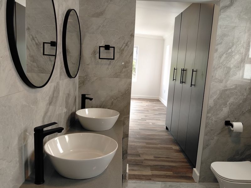 Modern bathroom featuring a double vanity with vessel sinks, matte black fixtures, and floor-to-ceiling cabinetry, finished with elegant marble-look wall tiles.