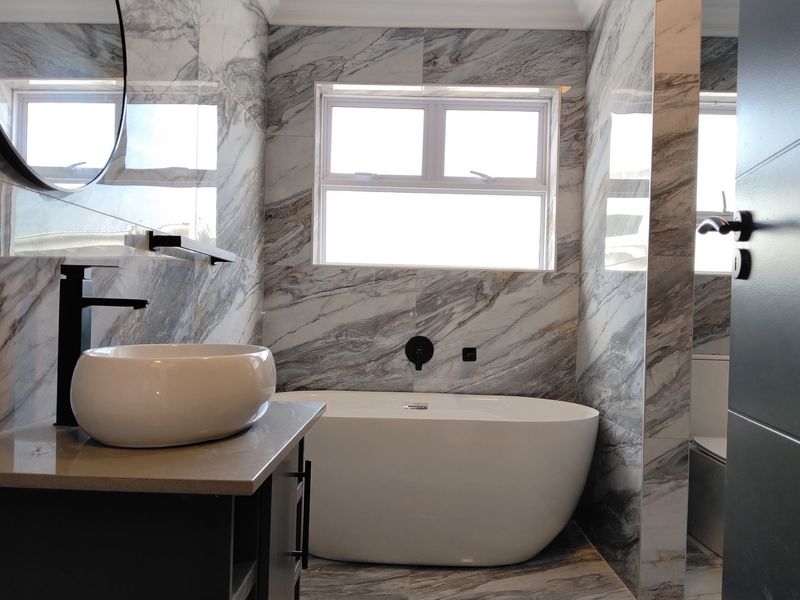 Modern bathroom featuring marble-look tiling, a sleek freestanding bathtub, a vessel sink vanity, and contemporary black matte fixtures.
