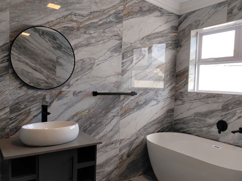 Modern bathroom featuring a freestanding bathtub, vessel sink on a vanity cabinet, and striking marble-look wall tiles with contemporary black matte fixtures.