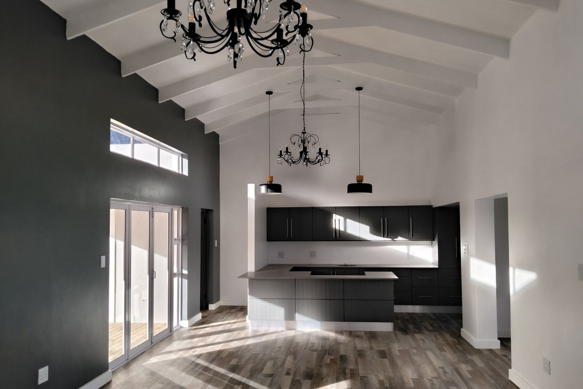 Spacious open-plan living and kitchen area featuring a high vaulted ceiling with exposed beams, modern dark cabinetry, and large bi-fold doors leading outdoors.