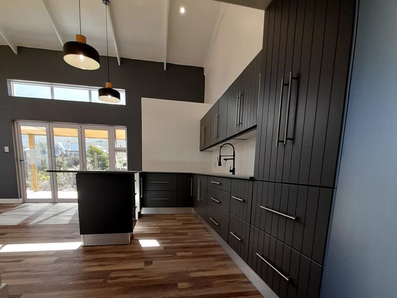 Modern kitchen featuring dark vertical-panel cabinetry, a central island, timber flooring, and a vaulted ceiling with contemporary pendant lighting.
