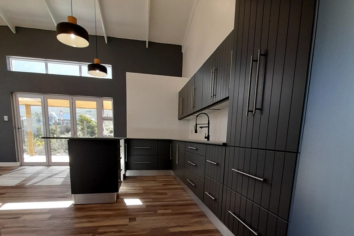 Modern kitchen featuring dark vertical-panel cabinetry, a central island, timber flooring, and a vaulted ceiling with contemporary pendant lighting.
