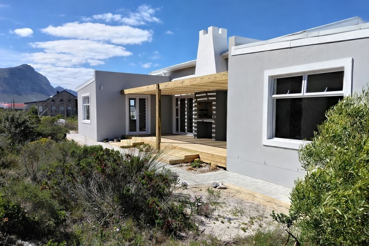 Rear exterior view featuring a wooden deck with a pergola, built-in braai, and modern grey facade with mountain views.