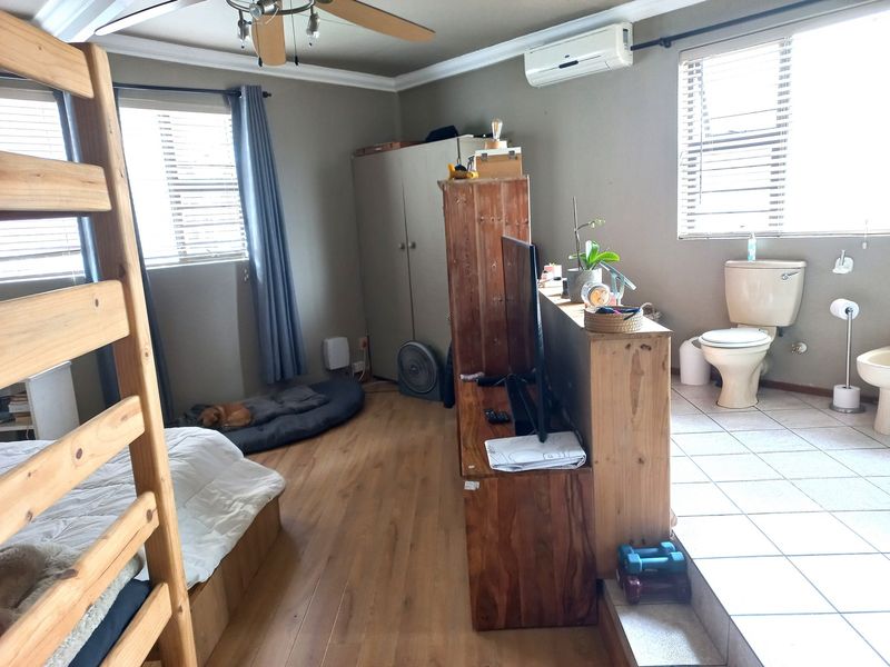 A bedroom featuring an open-plan layout with an integrated en-suite bathroom, split-system air conditioning, and a mix of laminate and tiled flooring.
