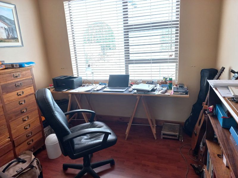 A functional home office space featuring laminate flooring and large window with venetian blinds, providing natural light for a productive work environment.