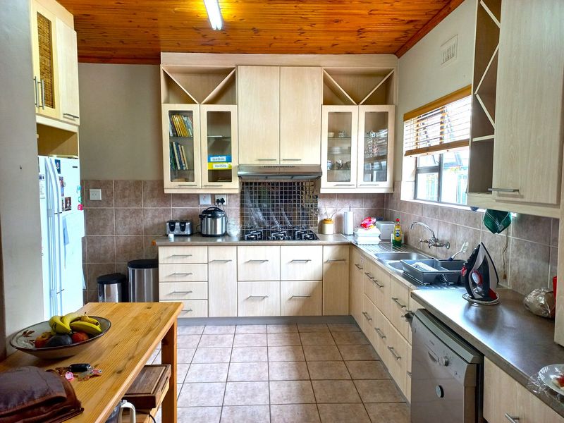 A functional kitchen featuring light-toned cabinetry, a gas hob with extractor fan, tiled splashbacks, and a timber-paneled ceiling.