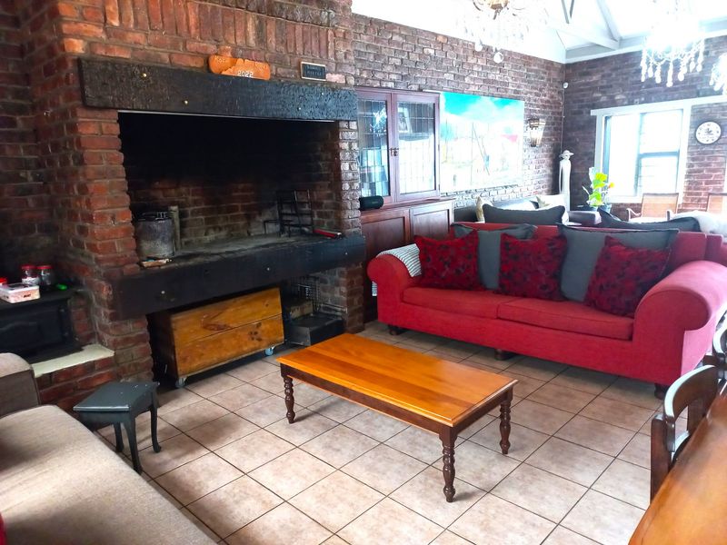 Spacious living room featuring a large exposed brick fireplace, vaulted ceilings, and tiled flooring, offering a rustic and cozy atmosphere.