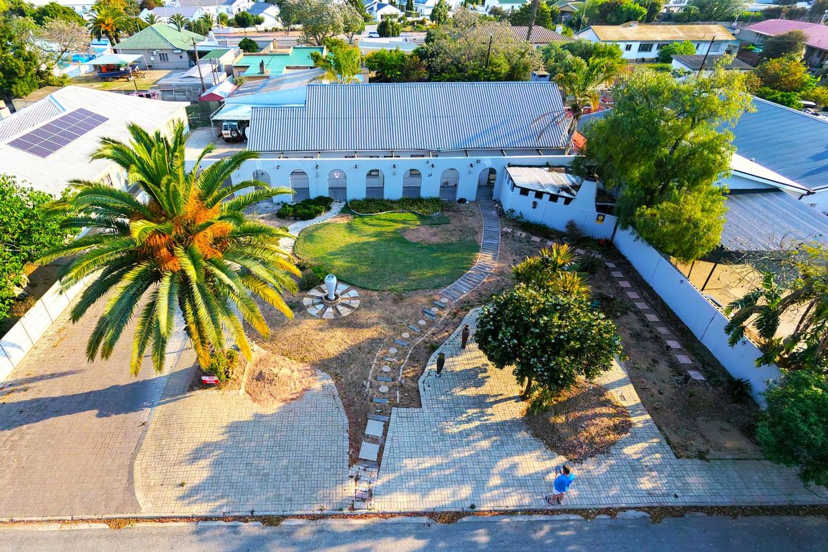 Aerial view of a residential property featuring a paved driveway, landscaped garden with a central lawn, and a building with an arched facade.