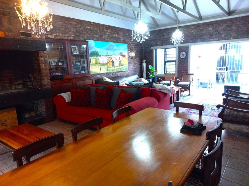 Spacious open-plan living and dining area featuring exposed brick walls, vaulted ceilings with exposed trusses, and a built-in fireplace, opening to an outdoor space.