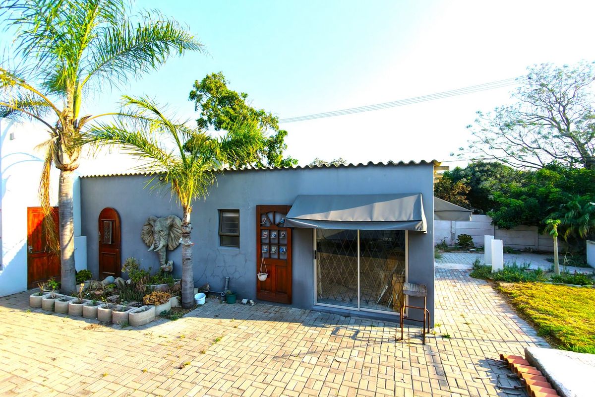 Rear exterior view of the property featuring a paved courtyard, sliding glass door with awning, and a secondary timber entrance door.