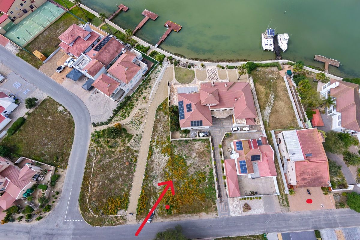 Aerial view of a vacant residential plot situated in a developed estate, featuring street access and proximity to the waterfront.