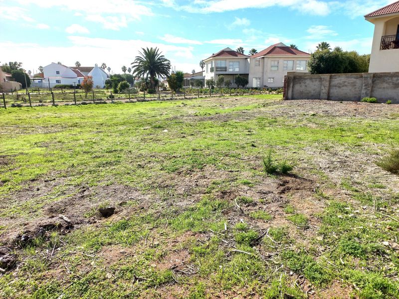 A vacant residential plot featuring a level grassed surface, enclosed by a boundary wall and wire fencing in a developed neighborhood.