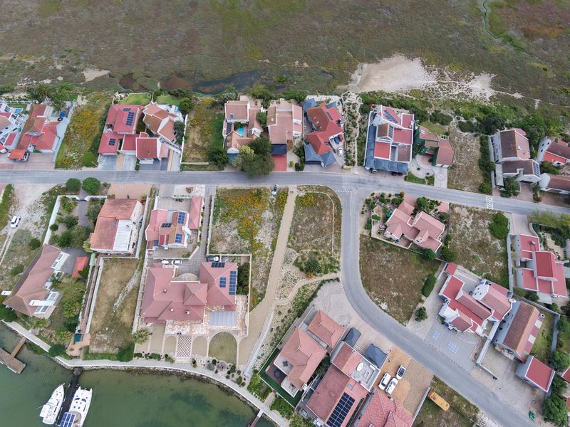 An aerial view of a residential estate featuring multiple homes with tiled roofs, solar panels, and direct access to the waterfront.