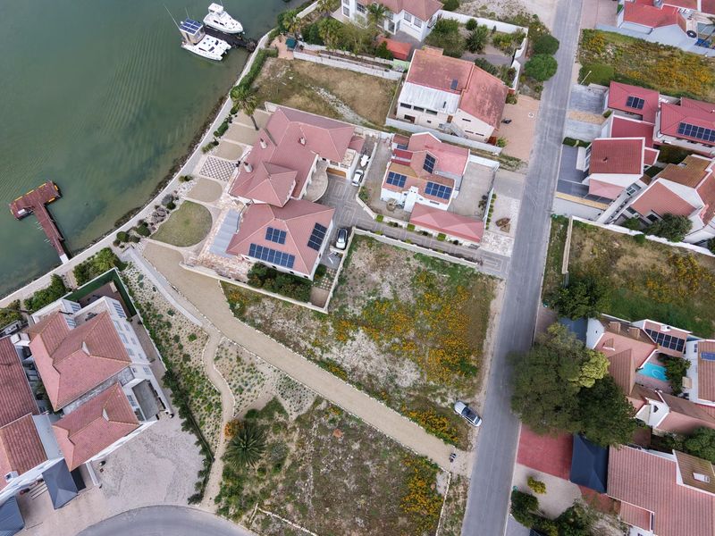 Aerial view of a residential property featuring solar panels, a paved driveway, and direct access to a private jetty on the waterfront.