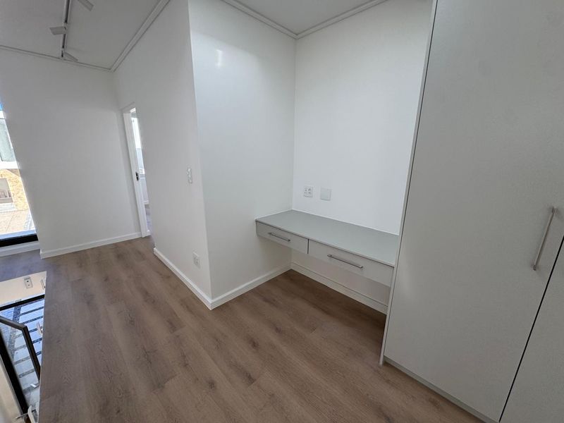 A bright, modern bedroom featuring laminate flooring, a built-in desk area, and a spacious built-in wardrobe with clean, minimalist finishes.