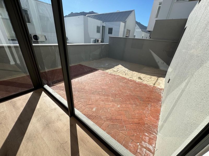 An outdoor patio area featuring herringbone brick paving and a section of exposed sand, accessible through large sliding glass doors.