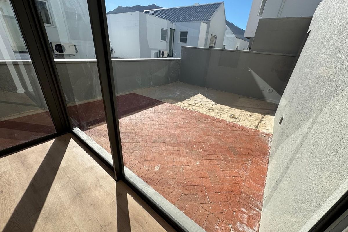 An outdoor patio area featuring herringbone brick paving and a section of exposed sand, accessible through large sliding glass doors.