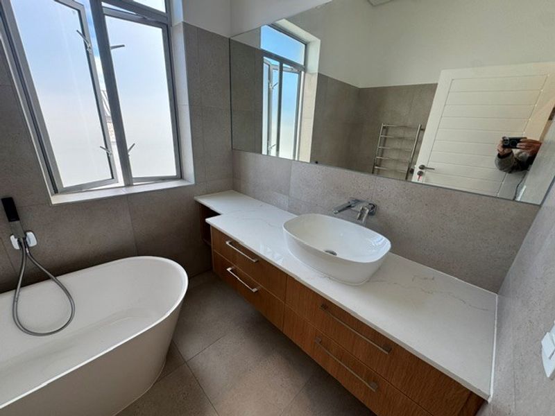 Modern bathroom featuring a sleek freestanding bathtub, vessel sink on a stone-topped vanity, large mirror, and heated towel rail with neutral tiling.