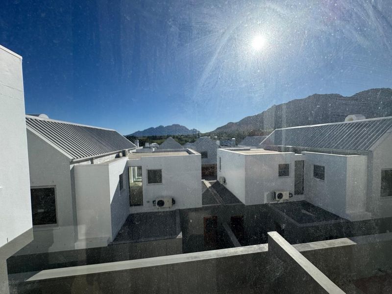 An elevated view overlooking a modern residential complex with white facades, metal roofing, and a scenic mountain backdrop.