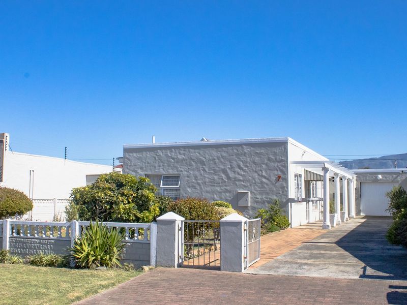Front view of a single-story house featuring a paved driveway, a covered pergola walkway, and a secure gated entrance with a well-maintained boundary wall.