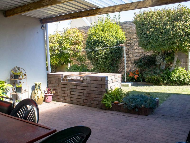 Covered outdoor patio featuring a built-in brick braai, paved flooring, and direct access to a private garden area with established landscaping.