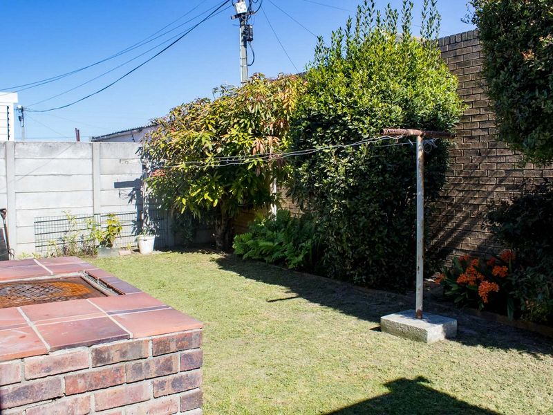 A private rear garden featuring a built-in brick braai area, established greenery, and a functional clothesline against a brick boundary wall.