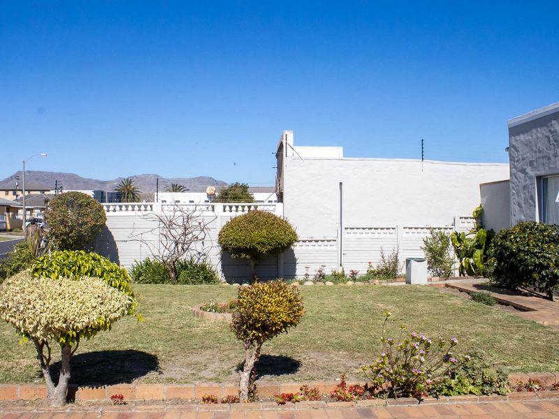 A well-maintained garden area featuring a lawn, manicured shrubs, brick-edged flower beds, and secure perimeter walling with electric fencing.