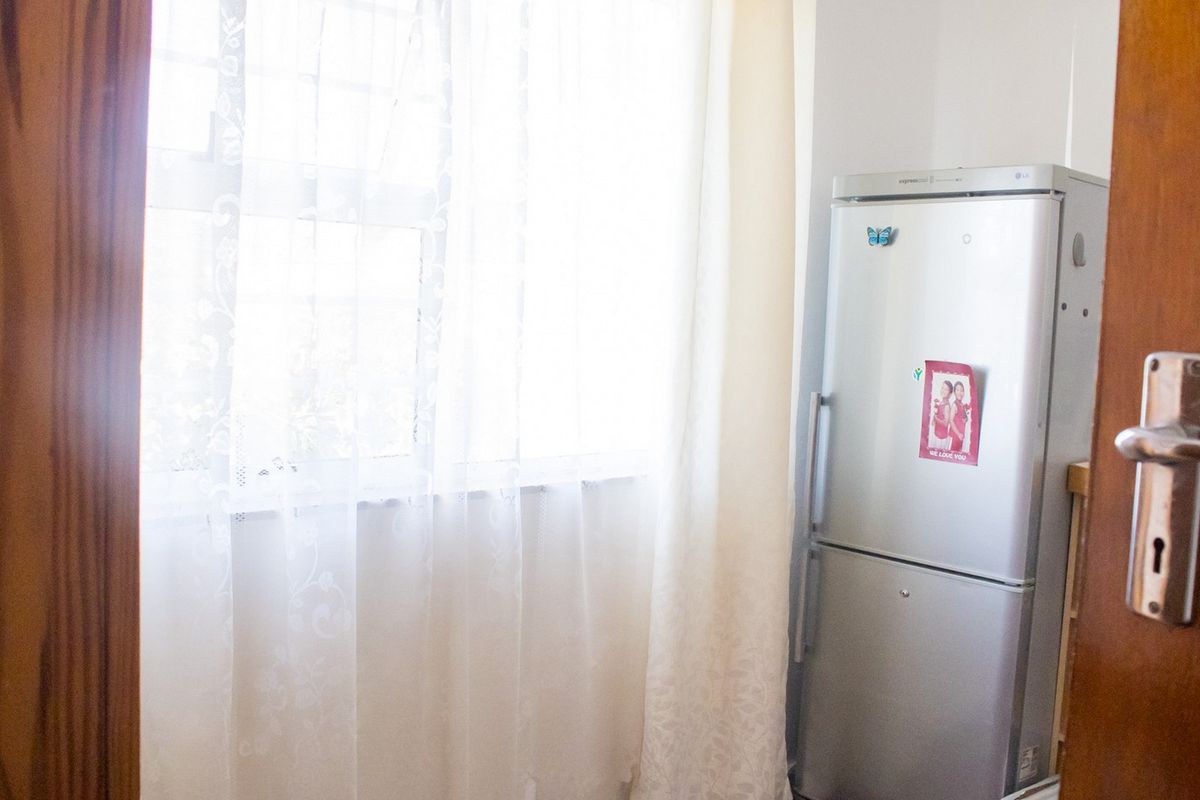 A view into a kitchen area featuring a window with curtains and a refrigerator.