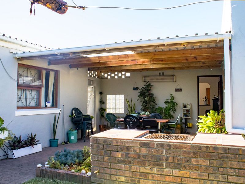 A covered outdoor patio area featuring a brick built-in braai, timber pergola roof, and paved flooring, ideal for outdoor entertaining.