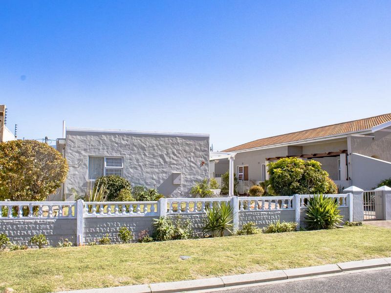 Front view of a residential property featuring a textured facade, tiled roof, and a low concrete boundary wall with a landscaped garden.