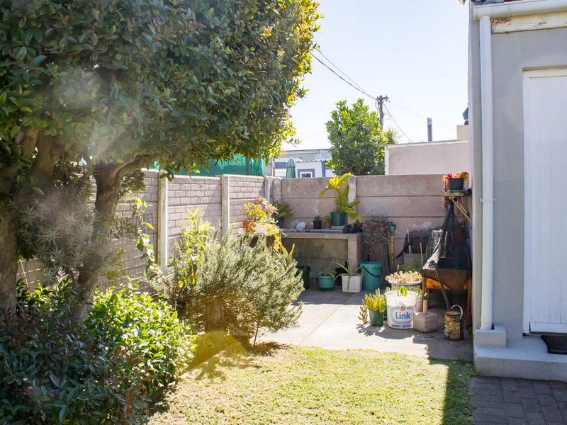 A rear garden area featuring a paved patio, a built-in concrete work surface, and a perimeter boundary wall.