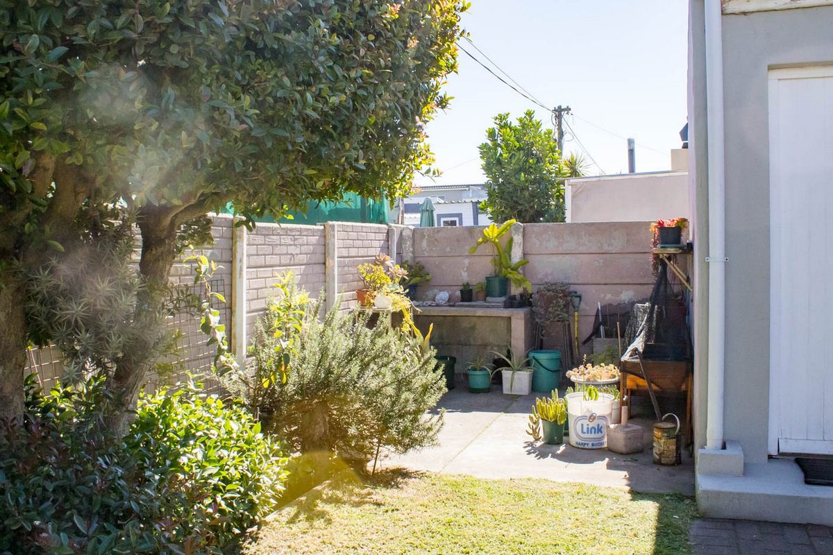 A rear garden area featuring a paved patio, a built-in concrete work surface, and a perimeter boundary wall.