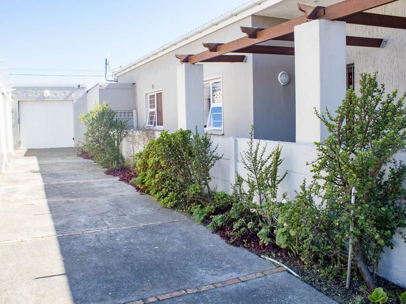 A view of the property's front exterior featuring a concrete driveway, a timber pergola structure, and a single garage door.