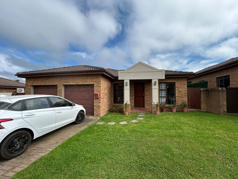Front elevation of a brick townhouse featuring a double garage, paved driveway, and a covered entrance porch with a landscaped front lawn.
