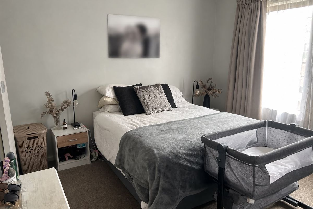A functional bedroom featuring neutral wall tones, carpeted flooring, and natural light provided by a window with installed curtain tracks.